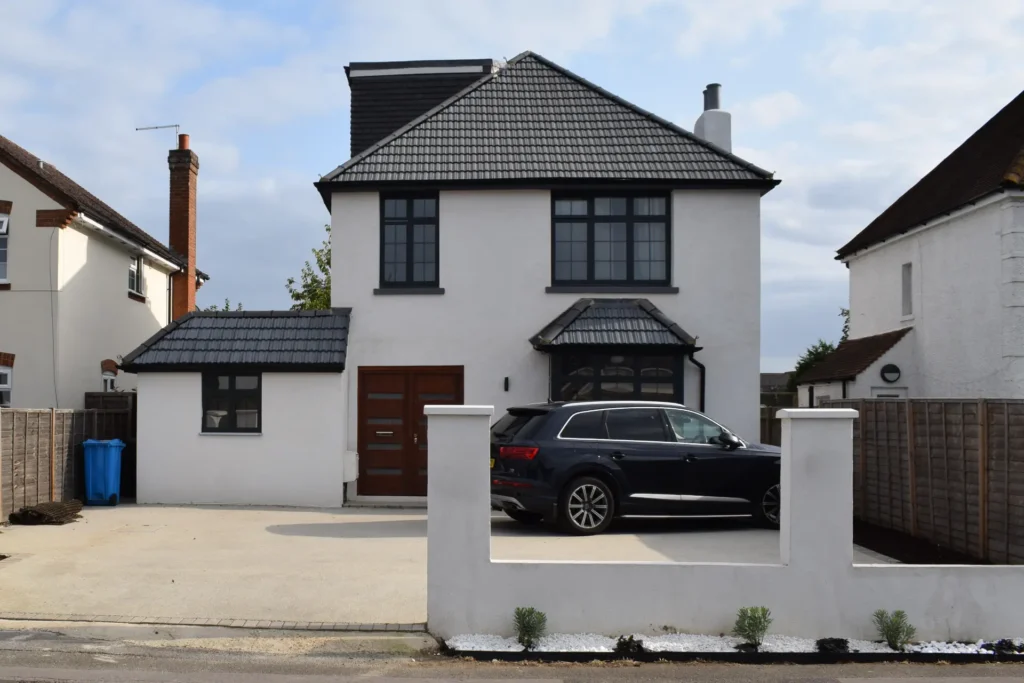 Two-story white house with dark tiled roof and large black-framed windows, a black SUV parked in the front driveway.